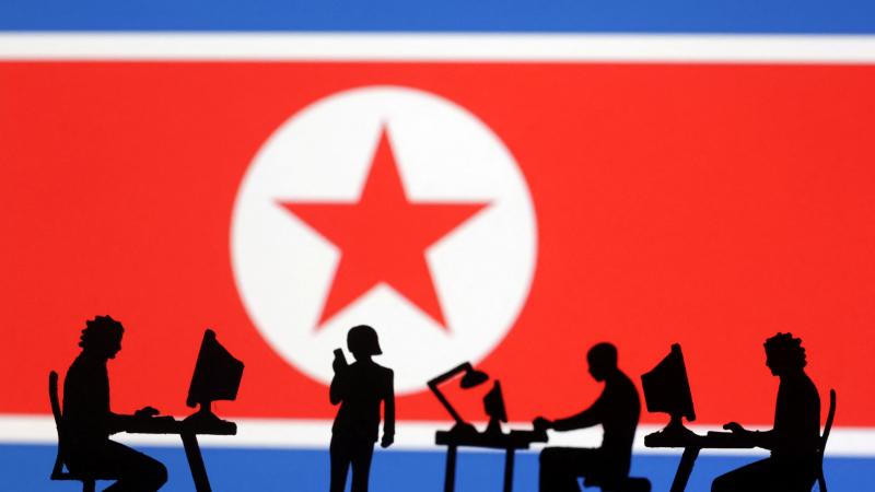 Ilustrācija, kurā cilvēki sēž pie datora Ziemeļkorajas karoga fonā